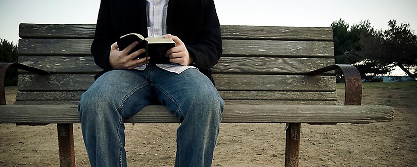 Man on bench reading a Bible
