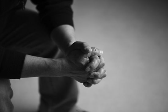 Man praying with hands clasped. Black and white photo.