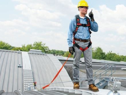 Safety worker talking on walkie talkie while anchored to rooftop with personal fall protection and engineered roofing system