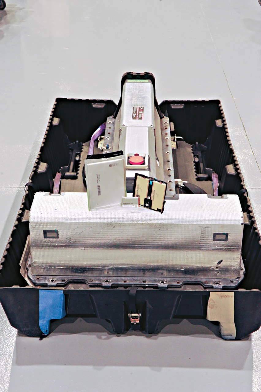 This photo shows a Chevy Volt battery pack and three small batteries propped up on top of it: one of the Volt battery’s 288 pouches along with batteries from a cell phone and an iPad.