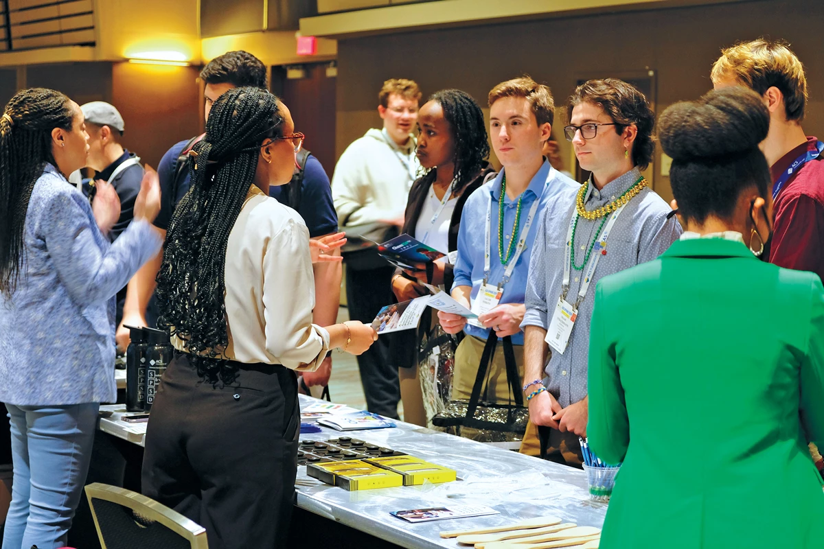 People talking around a table with pamphlets in their hands at a graduate fair.