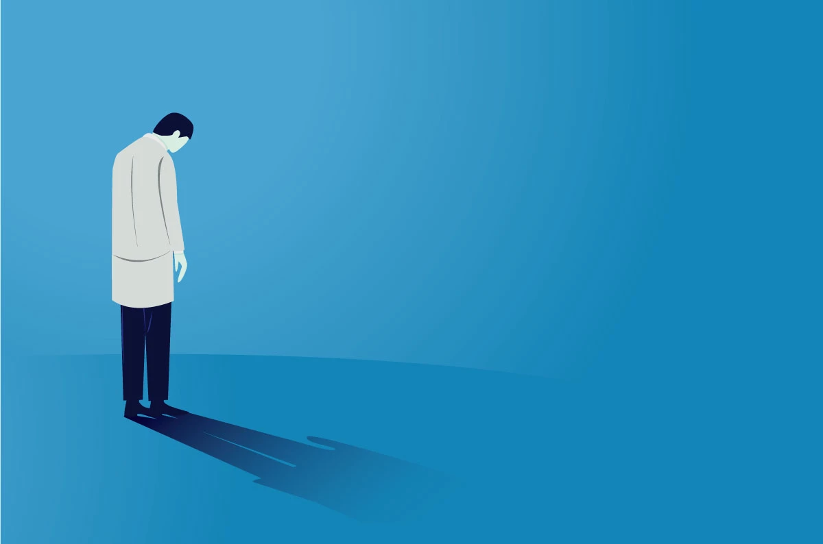 A person set against a blue background. Their head is looking to the ground and they look sad.