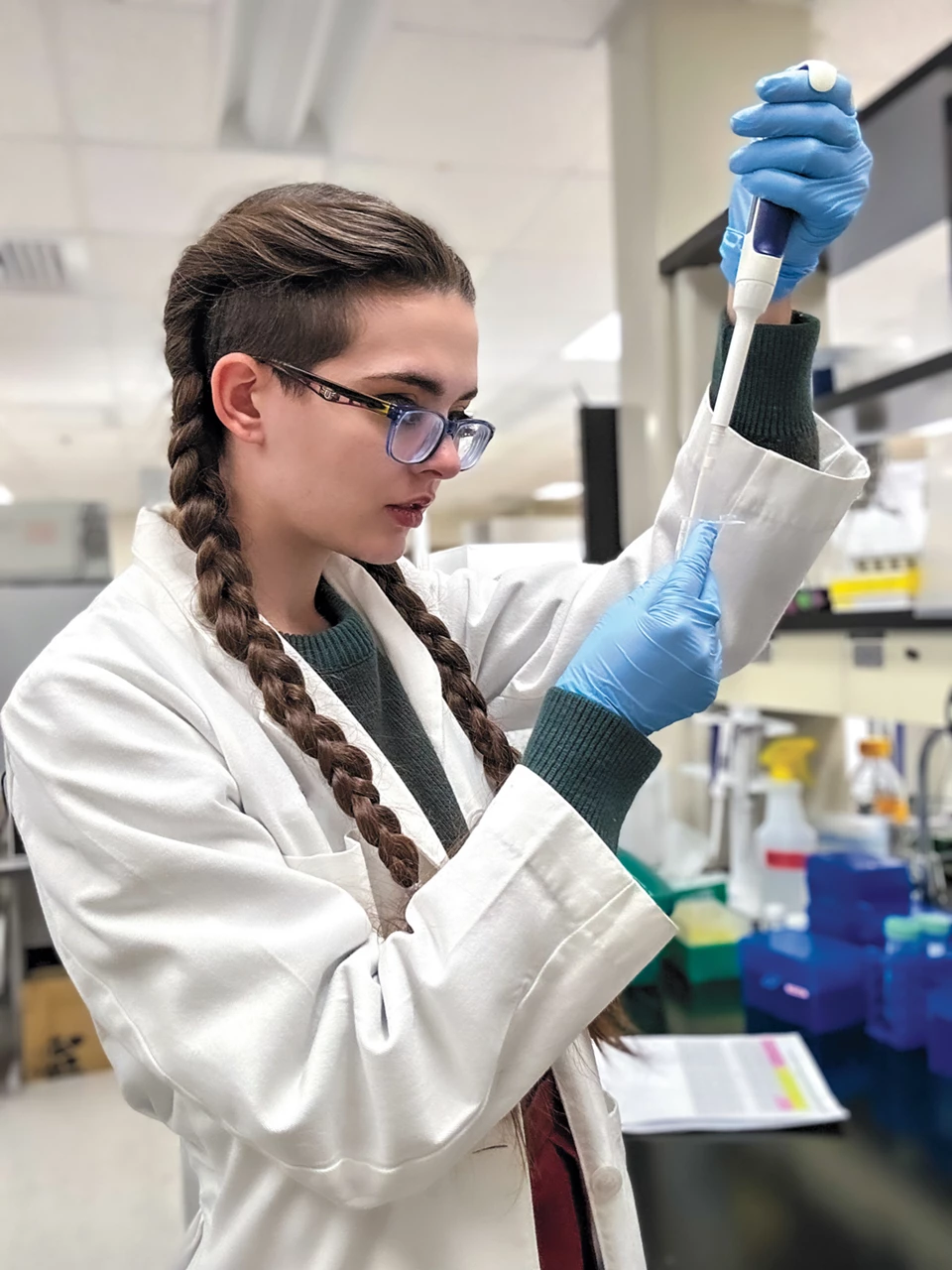 Kit Wallis is standing in a lab, pipetting ammonium bicarbonate into a small centrifuge tube.
