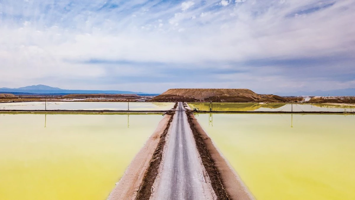 Photo of rectangular lithium evaporation ponds arranged in a grid and filled with yellow-green liquid. The ponds are surrounded by a desert and mountains.