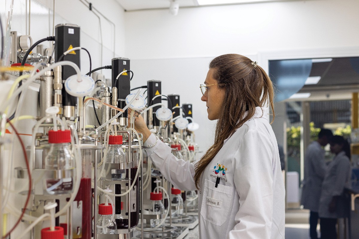 A scientist in a white lab coat uses a fermenter in a laboratory. 