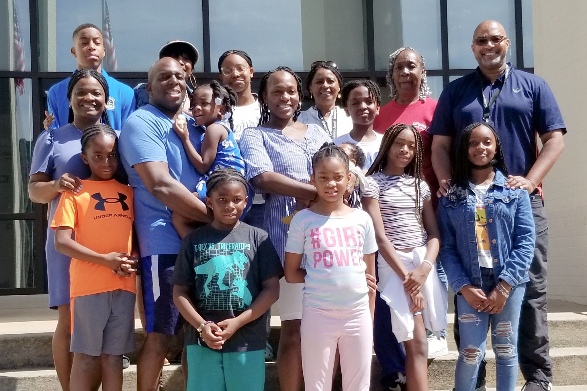 Large family group of adults and children posing together outside a building on a sunny day