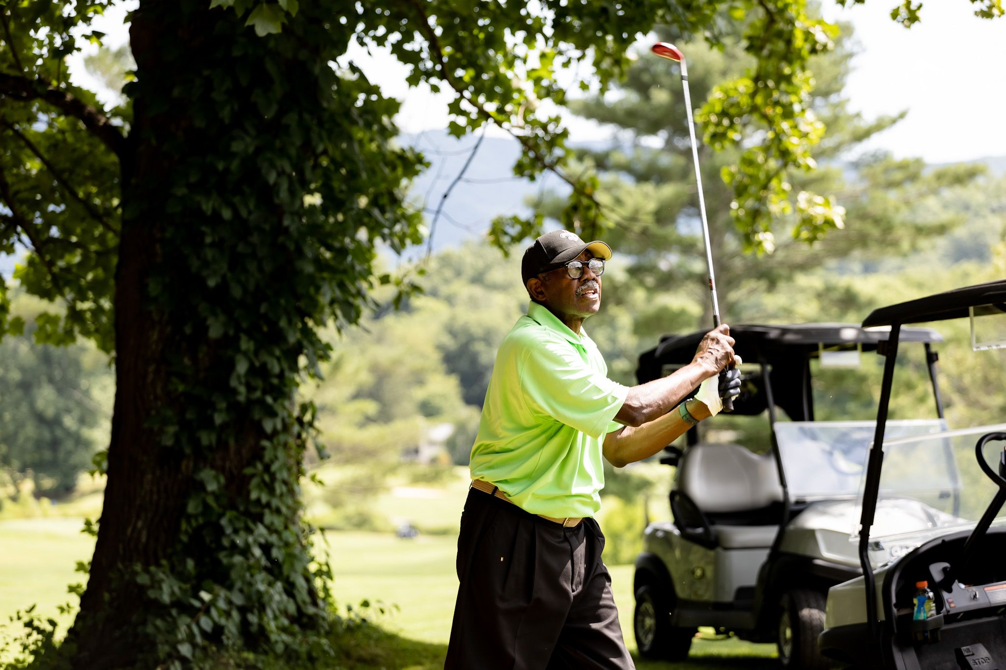 Man in a bright green shirt swings a golf club on a sunny day