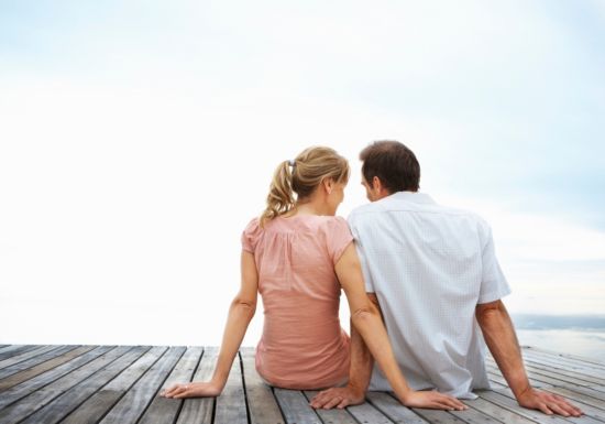 Husband and wife sitting on dock by water.