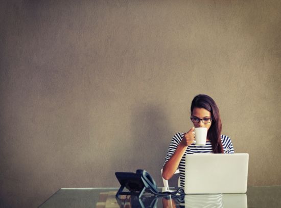 Young woman drinking coffee at her desk in front of her computer