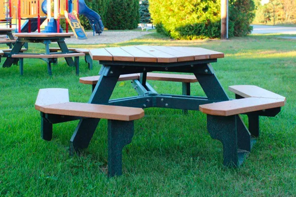  USA-made Polly product table with attached benches on green lawn, near a colorful playground and surrounded by trees.