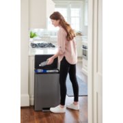 woman in kitchen throwing water bottle into dual stream step-on recycling can image number 6