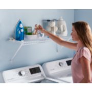 Woman using Rubbermaid organizing wire shelf mounted above washer and dryer in laundry room image number 6