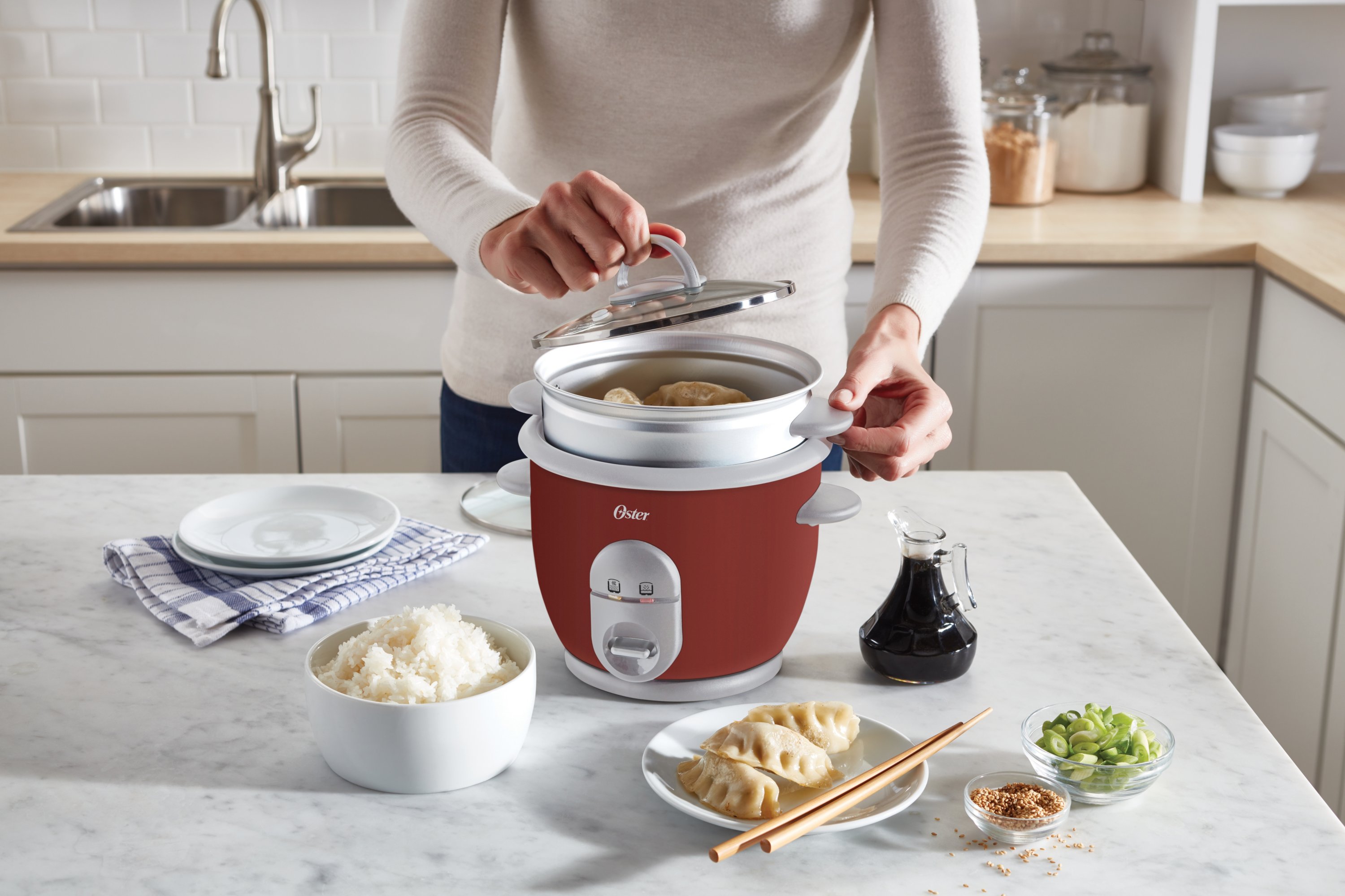 https://s7d9.scene7.com/is/image/NewellRubbermaid/4722000000-oster-rice-cooker-with-steamer-red-angle-lifestyle-with-talent-1