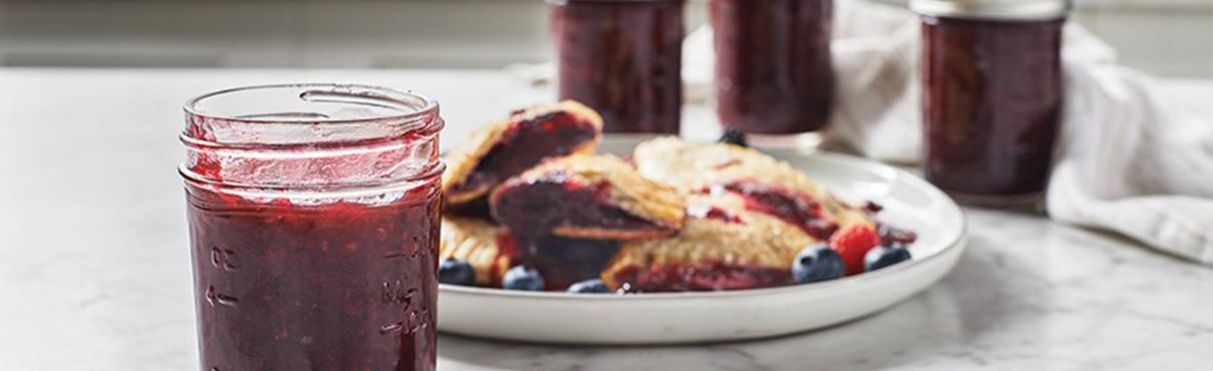 Ball jar filled with fruit preserves in foreground with toast and jam in background