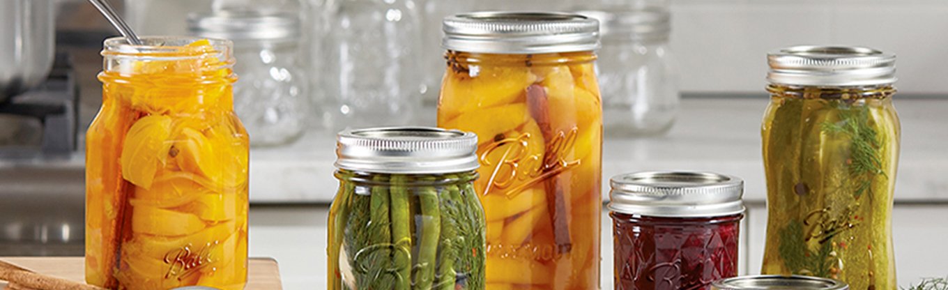 Array of Ball jars on kitchen counter with preserved fruit and pickled vegetables