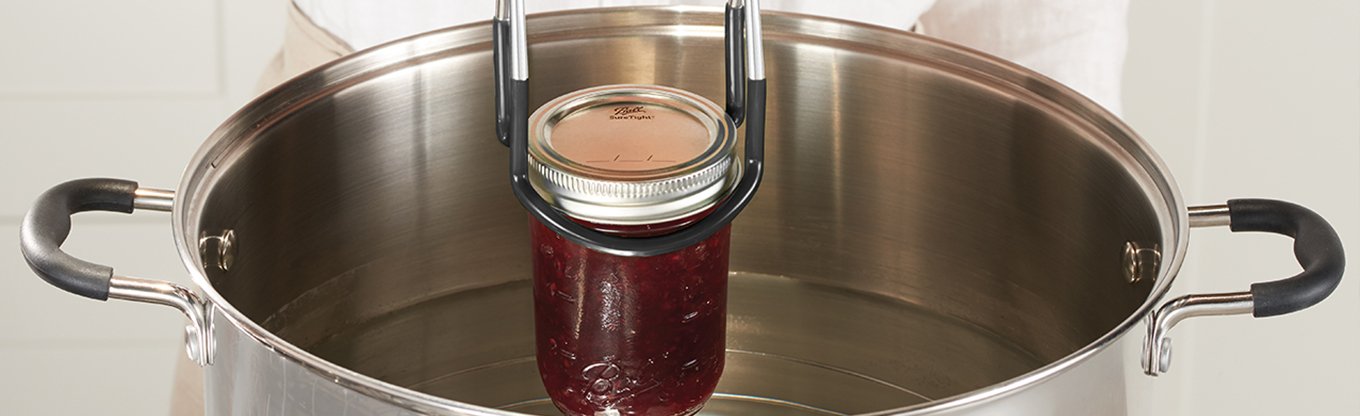 Ball jar being submerged in pot of water with safety tongs
