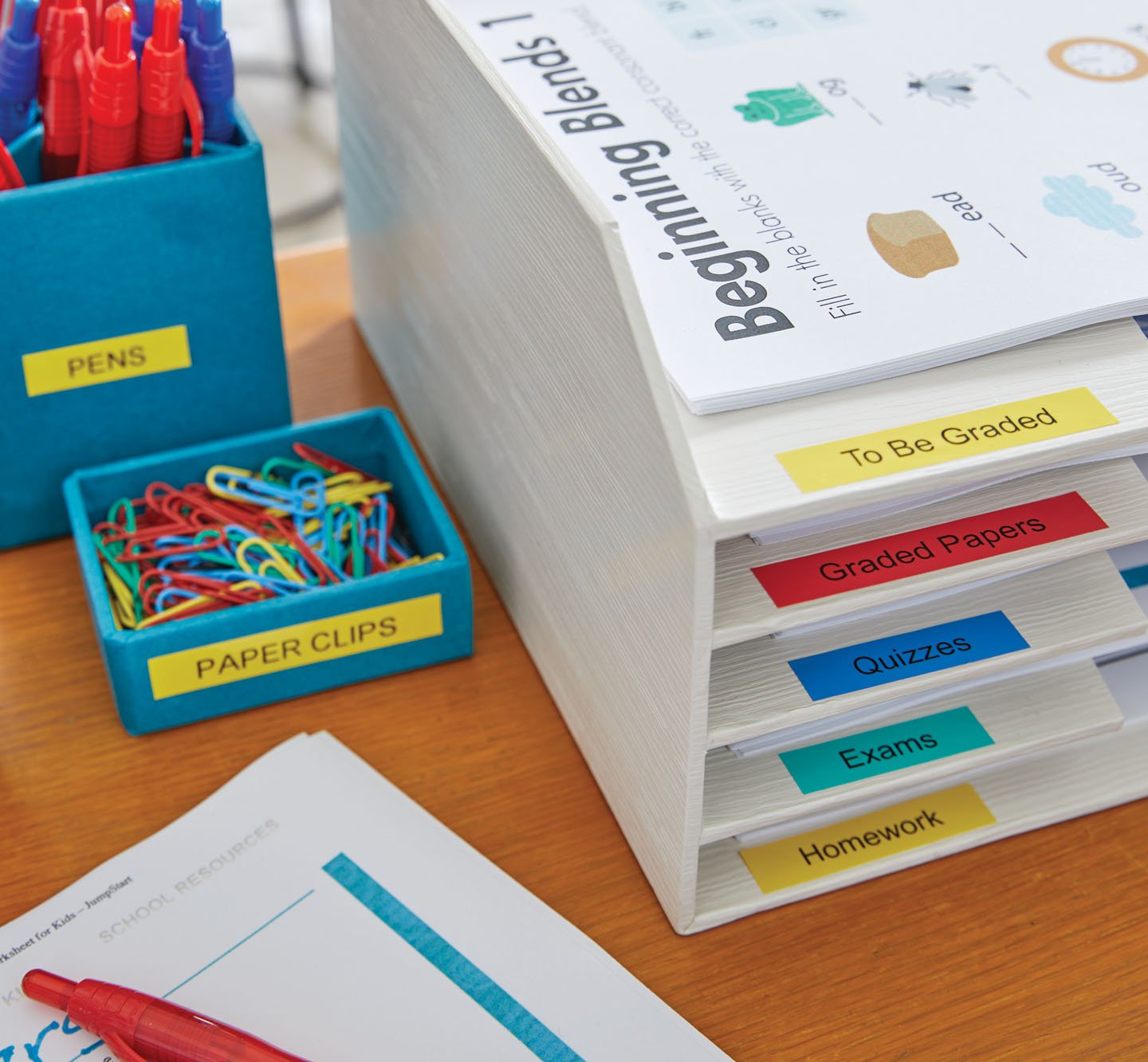 A desk with colorful labels on a desk organizer, paper clip holder and pen holder.