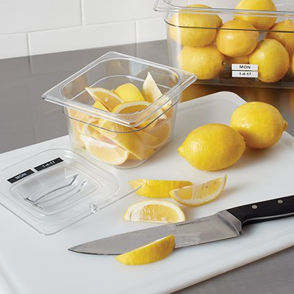 A labeled bin of lemons near a chopping board.