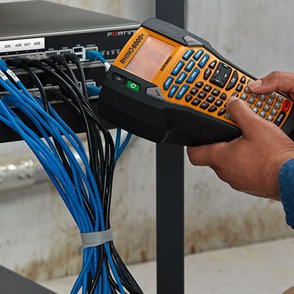 A person using a Rhino 6000 plus label maker to create a label for an electronic wiring panel.