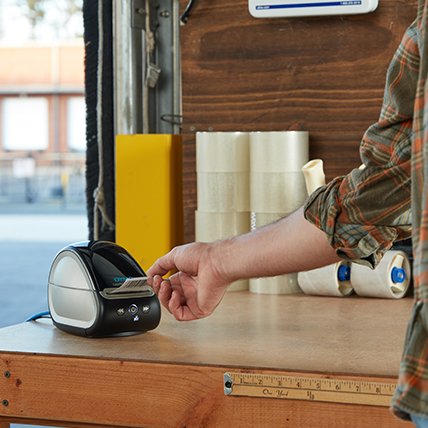 A hand reaching for a printing label from a Label Writer.