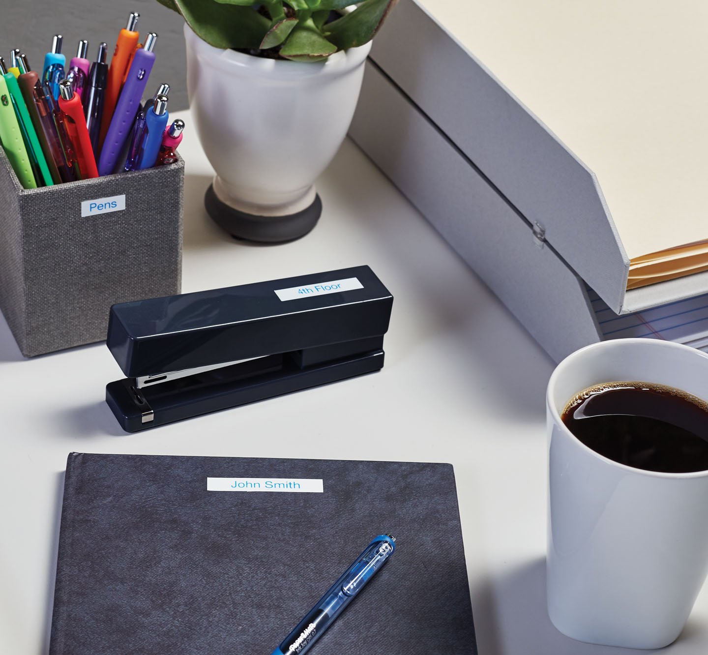A labeled notebook, stapler and pen holder on a desk.