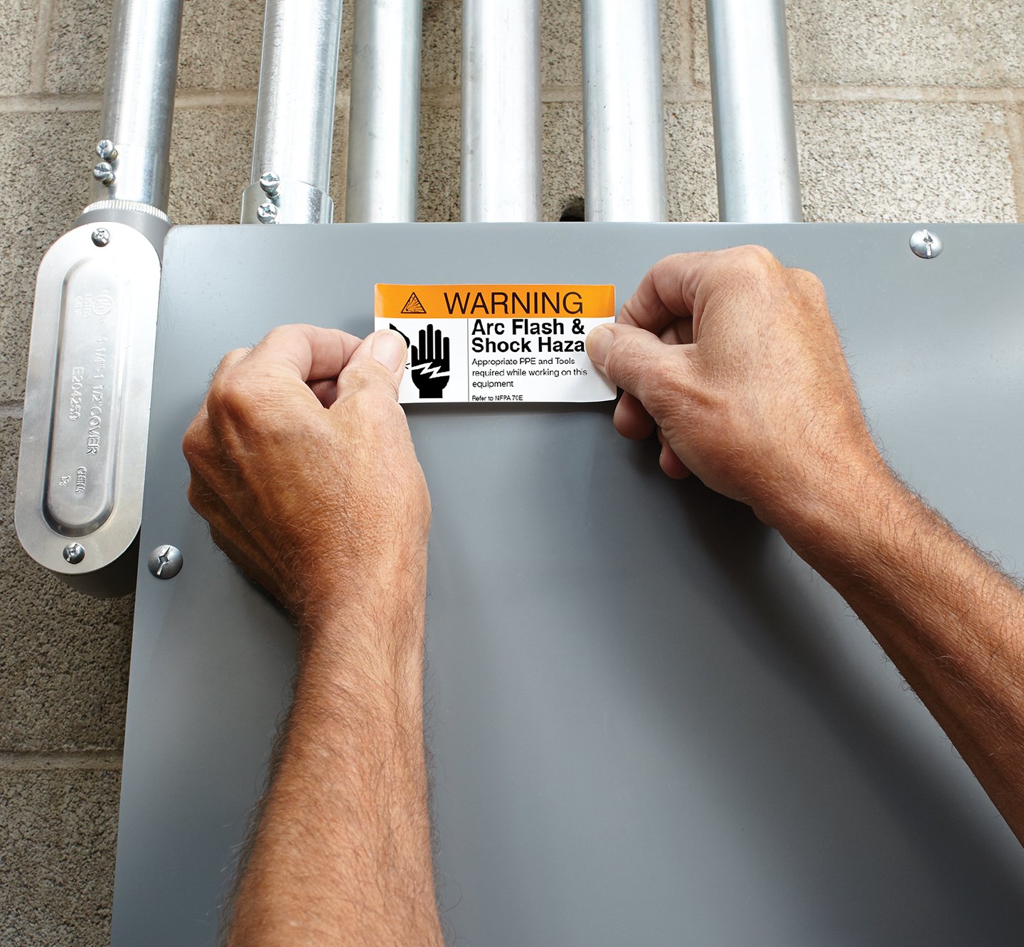 Hands placing a warning label on an electrical box.