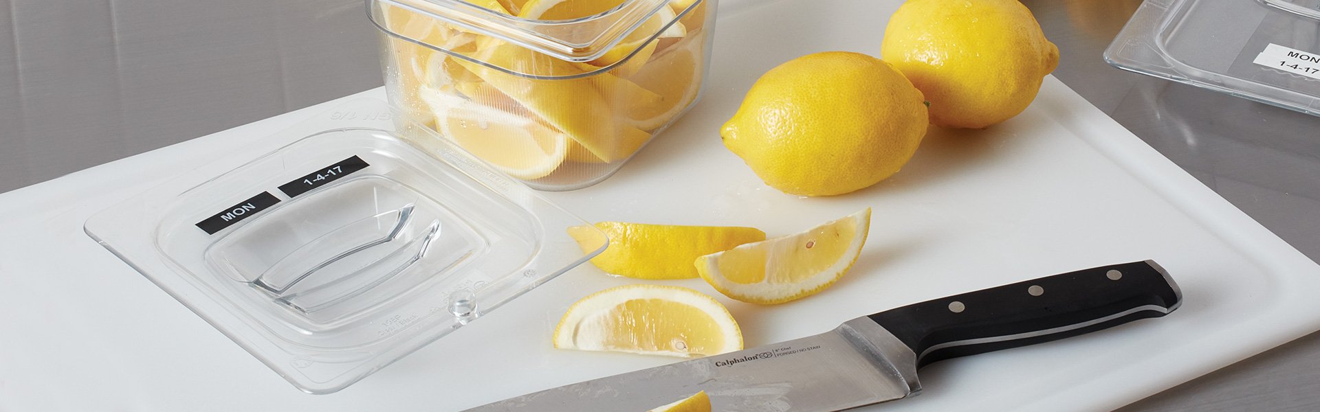 A labeled bin of lemons near a chopping board.