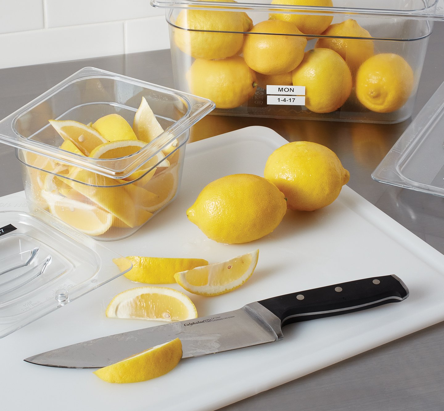 A labeled bin of lemons near a chopping board.