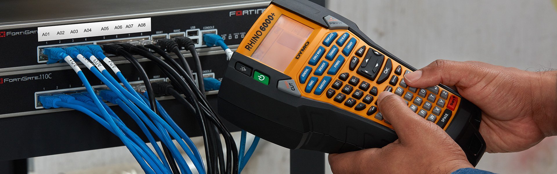 A person using a Rhino 6000 plus label maker to create a label for an electronic wiring panel.