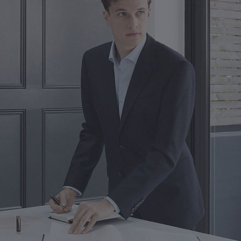 A man in a suit using a Duofold Classic pen to write in a notebook.