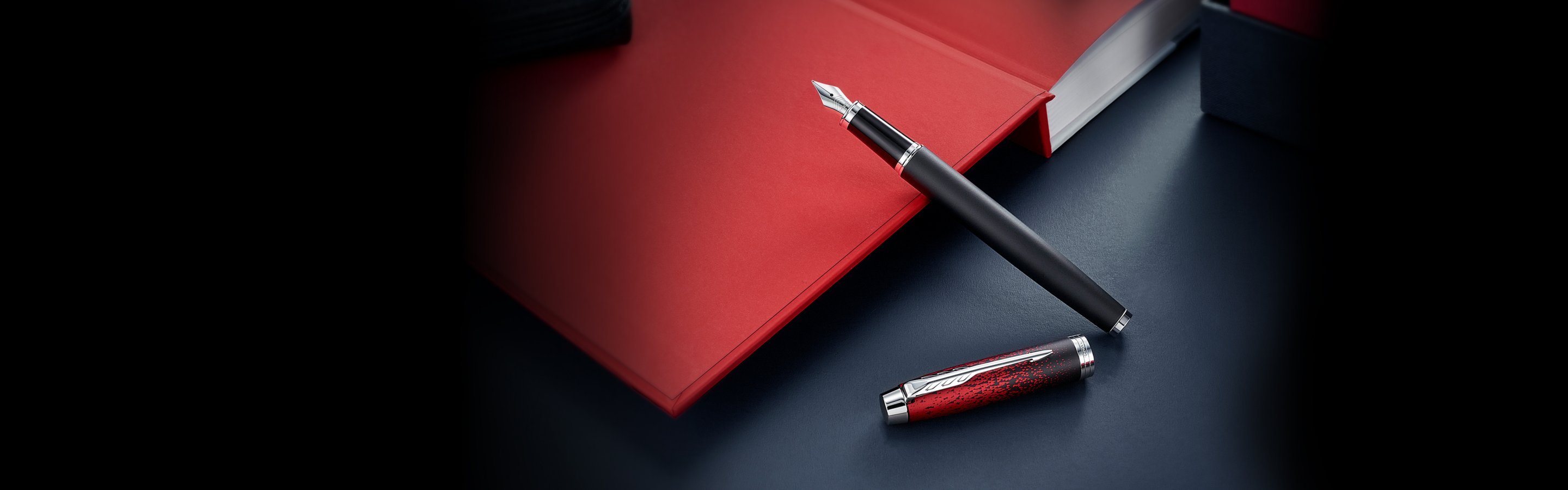 An uncapped Parker IM special edition red ignite fountain pen leaned against an opened book cover.
