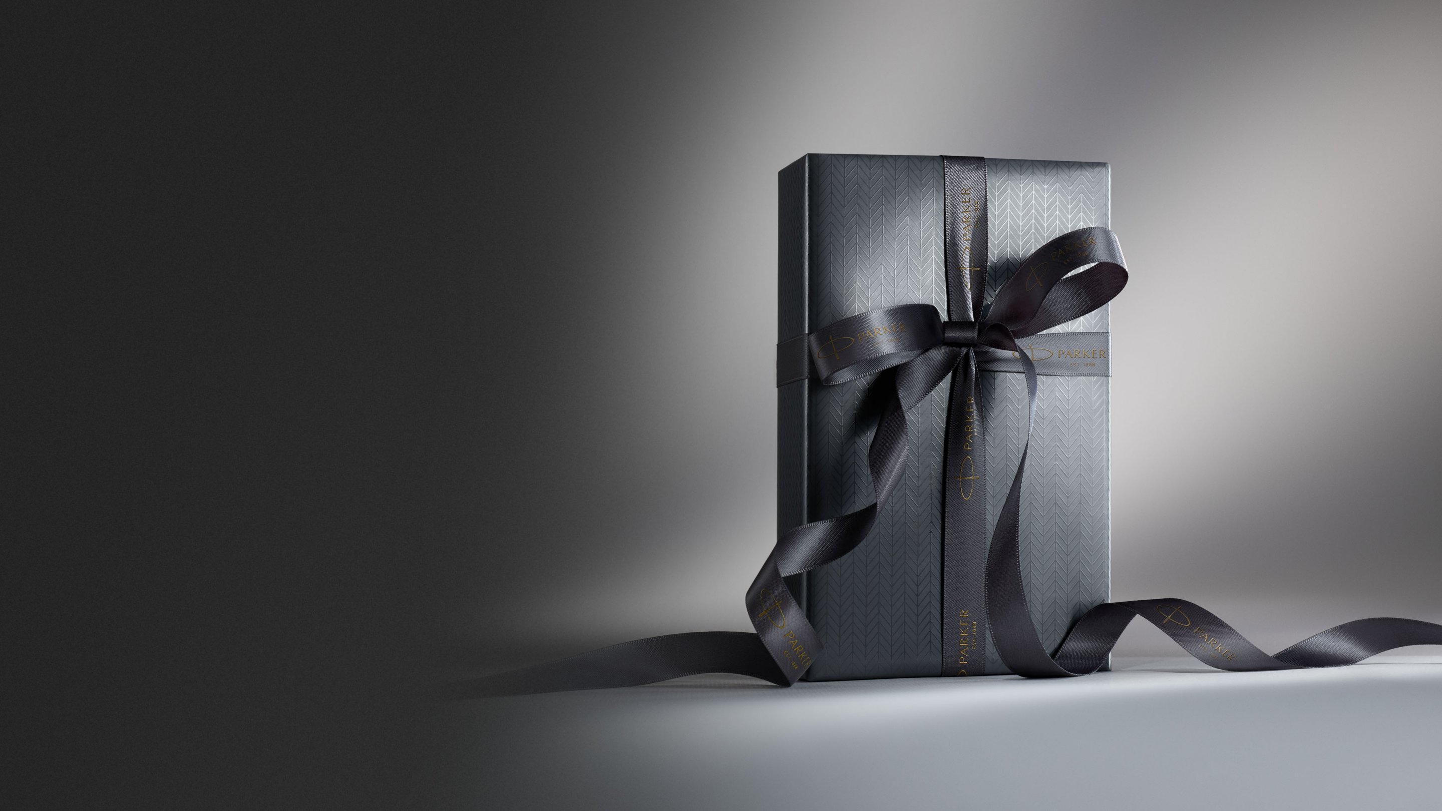 A gift box with a ribbon bow stood upright under a spotlight.