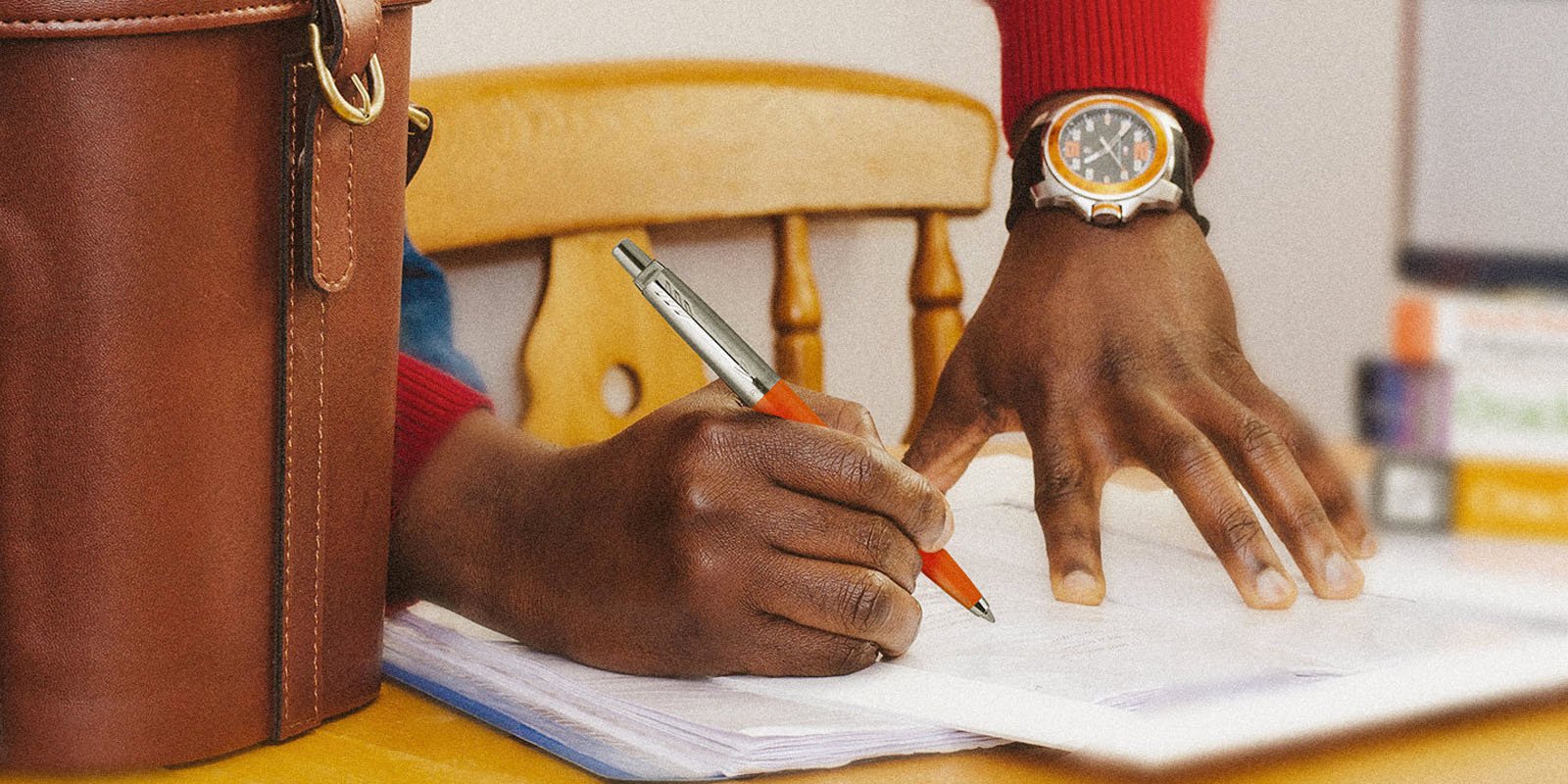 Closeup of a hand holding a Jotter Originals in orange finish and writing in a notebook.
