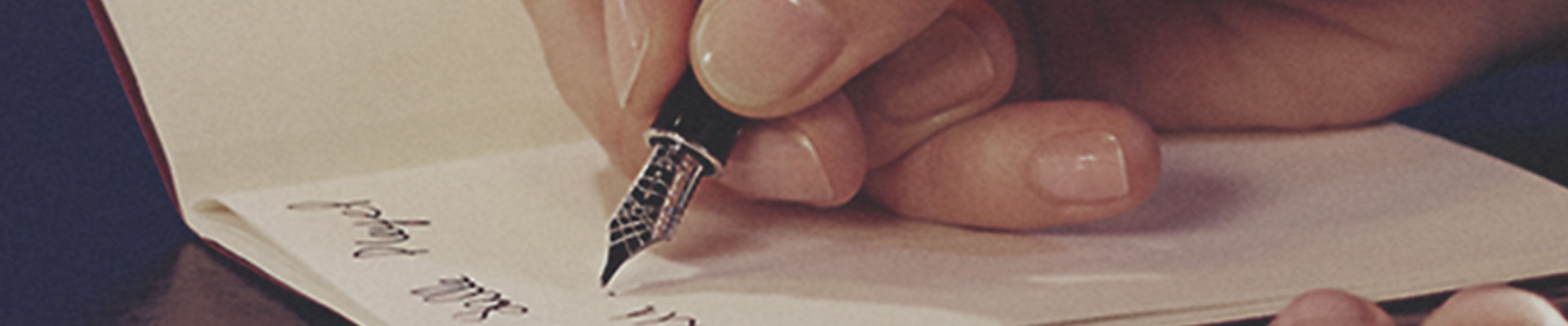 Closeup of a hand using a fountain pen to write in a notebook.
