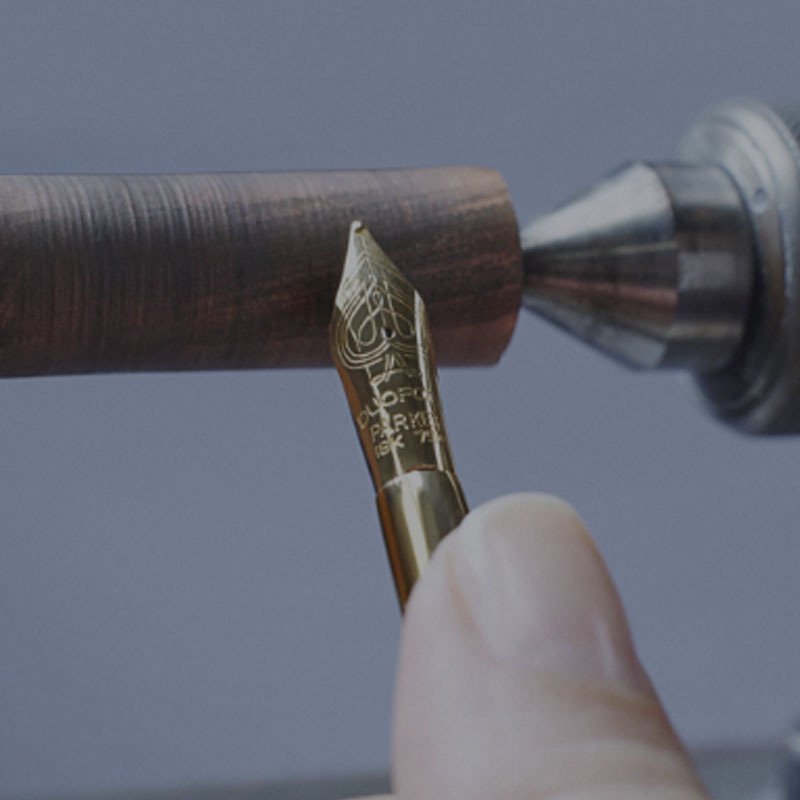 A hand shaping a fountain pen nib against a wooden cylinder.