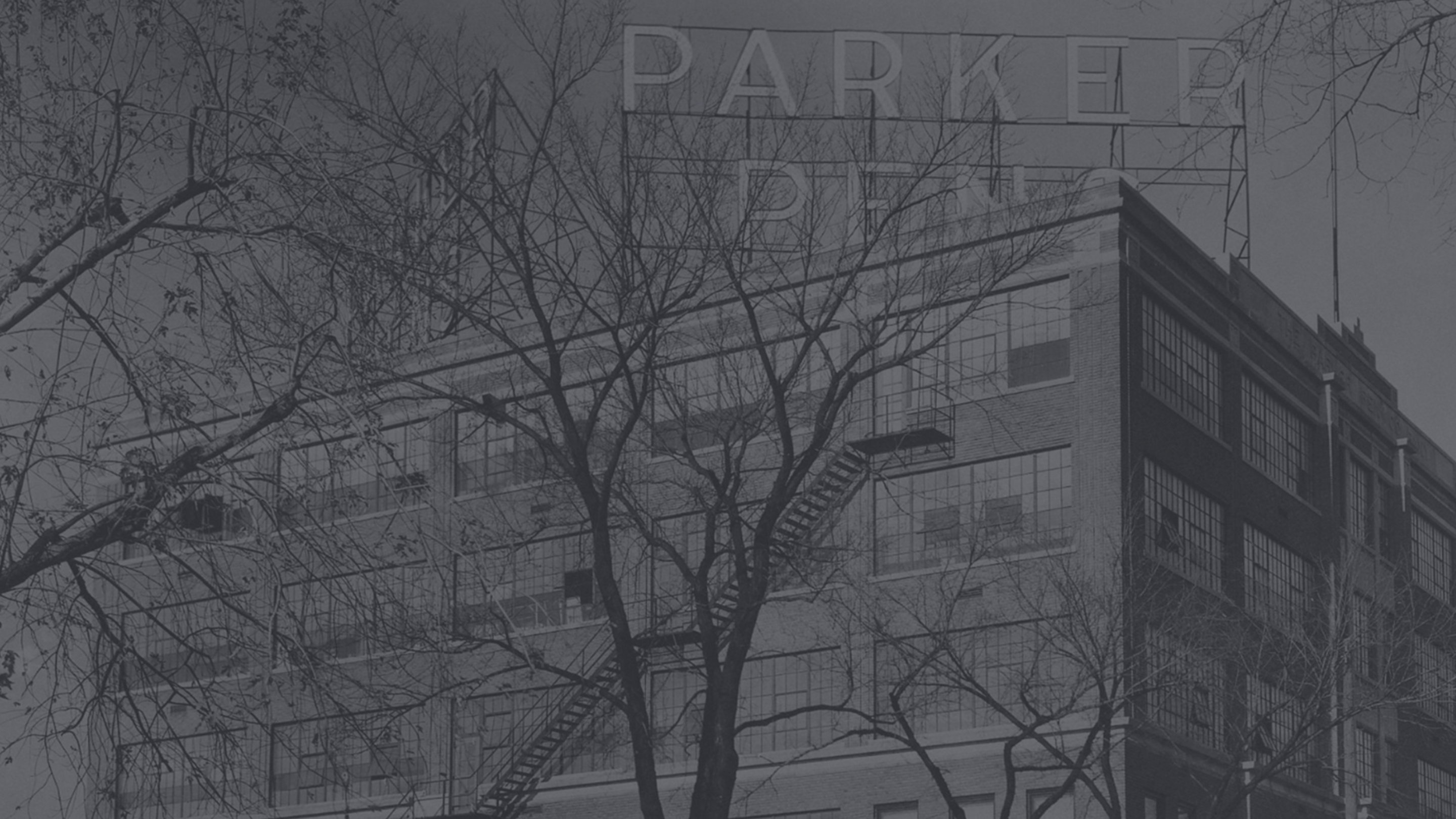 A vintage photo of a Parker pen factory behind bare trees.