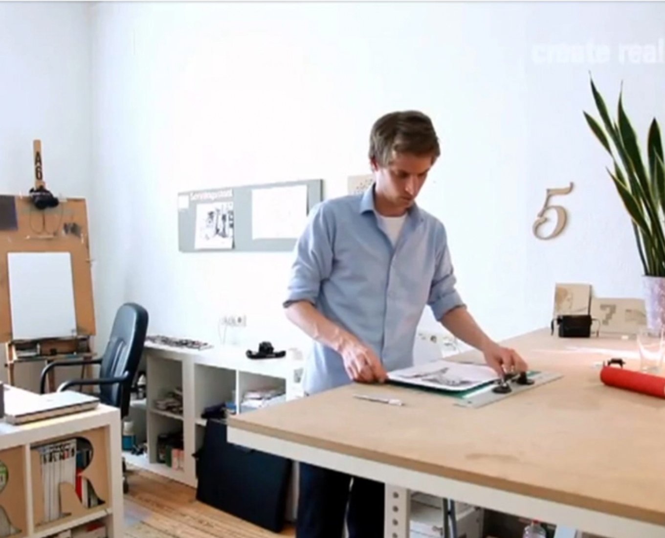 A photograph of a man standing at a desk and looking at a drawing.
