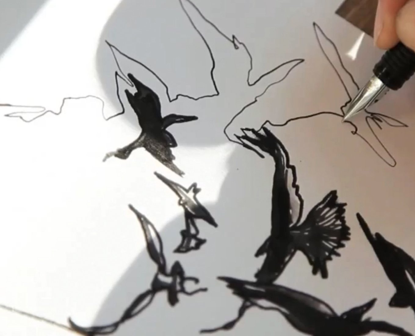 Closeup of a pen nib drawing birds in flight.