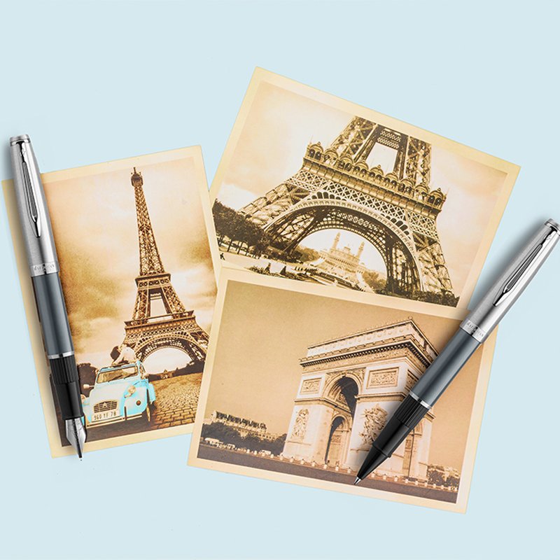 An Embleme fountain pen and rollerball pen laid over sepia tone pictures of the Eiffel Tower and Arc de Triomphe.
