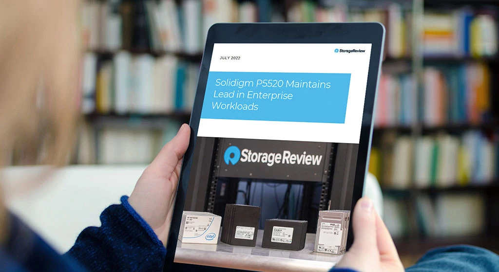 Person holding a tablet computer showing StorageReview article about the Solidigm P5520, which maintains lead in enterprise workloads for SSDs