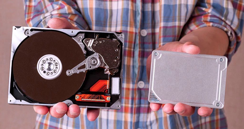 Man holding an SSD solid state and an HDD spinning disk comparing the size and inner workings of hard drive with smaller SSD size for compact sotrage