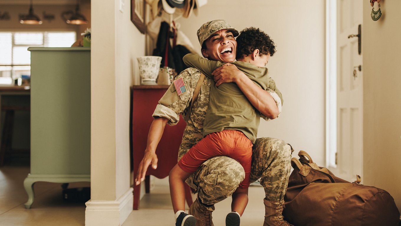 Soldier embraces child in homecoming moment inside foyer in house