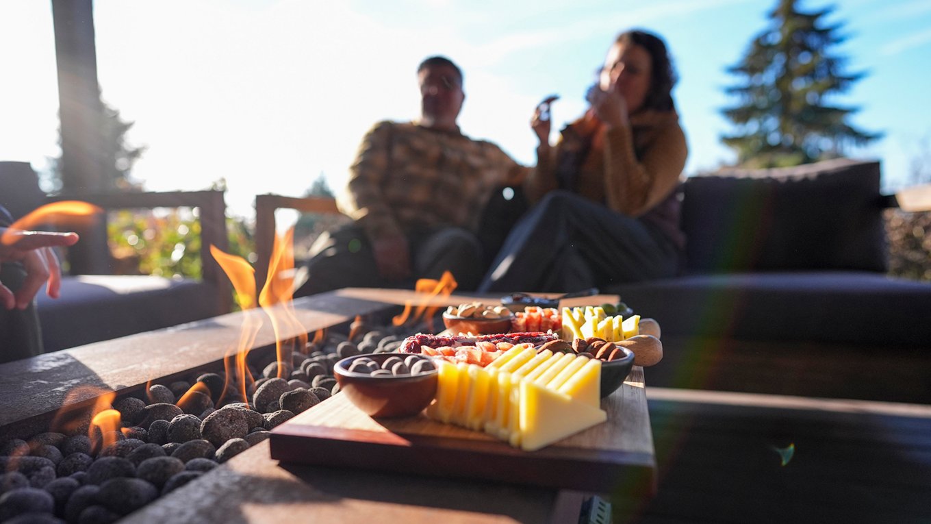 couple sitting on couch by small standing stones fireplace, enjoying charcuterie board
