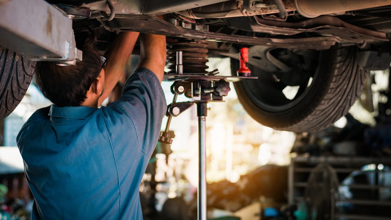 Mechanic repairing a car, Mechanic inspects car suspension system and chassis with a torch-lite under the car.