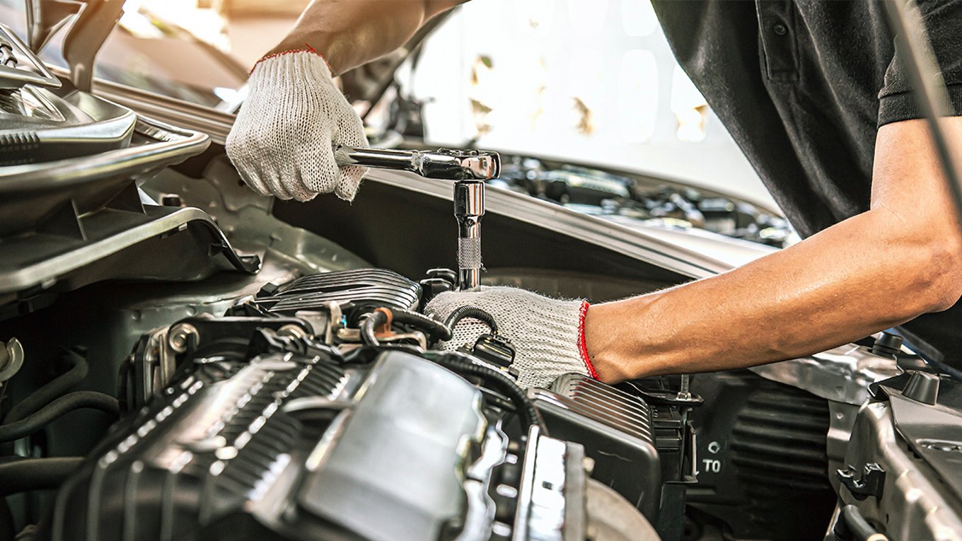 arms of auto mechanic using tool on engine of car