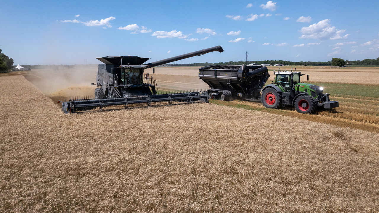 Combine harvester unloading grain into a tractor and grain cart during harvest in a crop field.