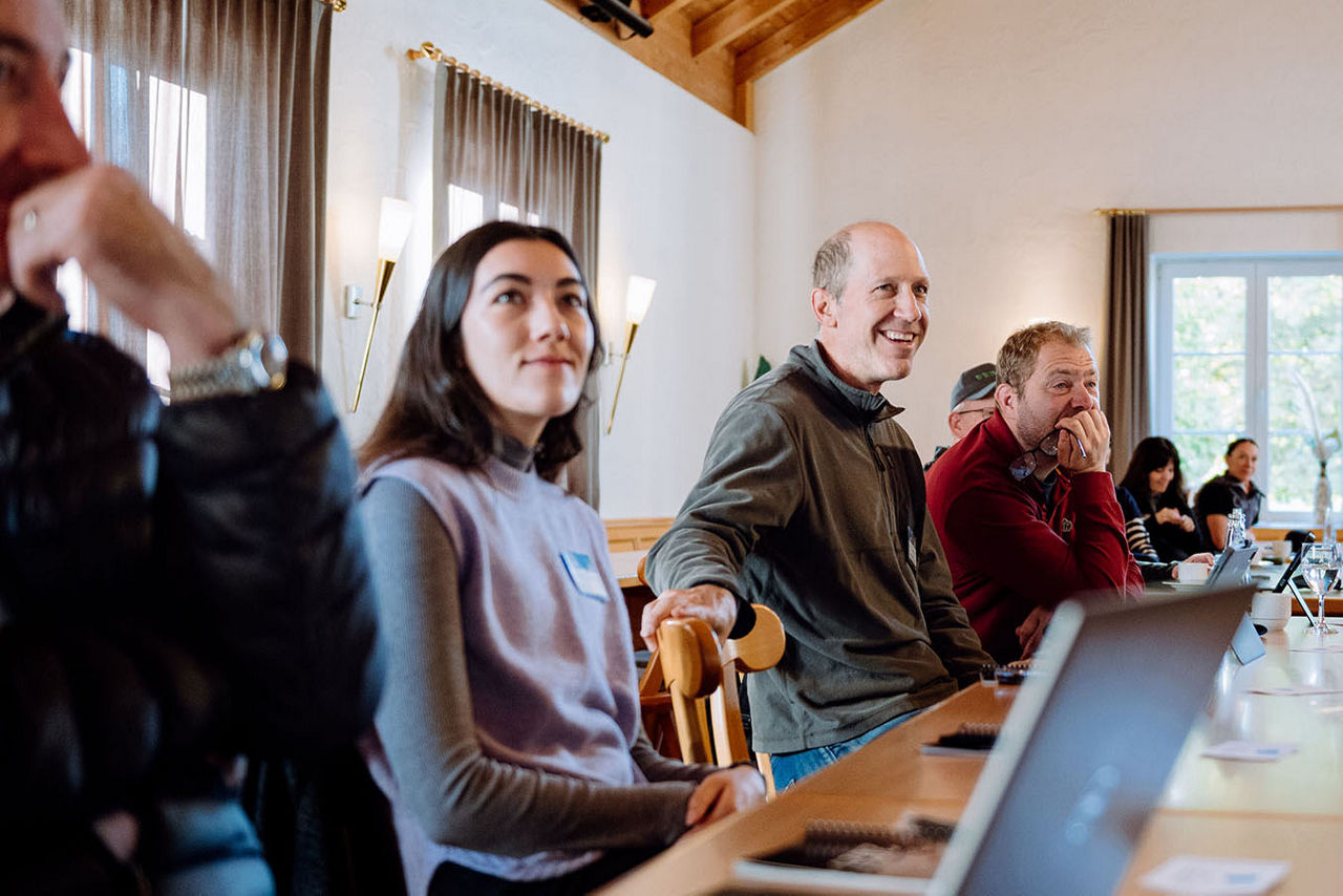 People gathered around a table in a meeting room with laptops and notepads, looking engaged.-Alt-text description generated by Azure Vision AI model