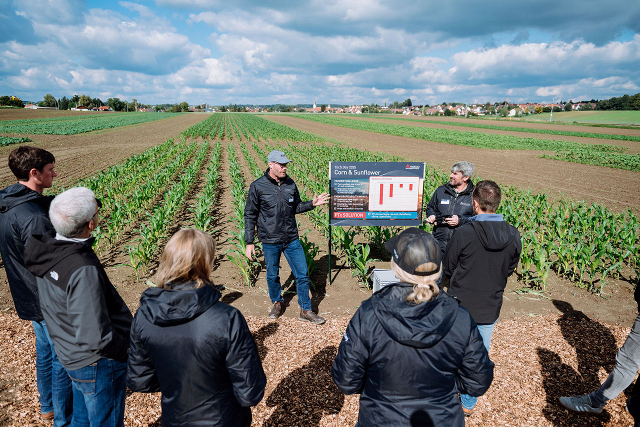 A group of people attentively listening to a presentation in a cornfield.-Alt-text description generated by Azure Vision AI model