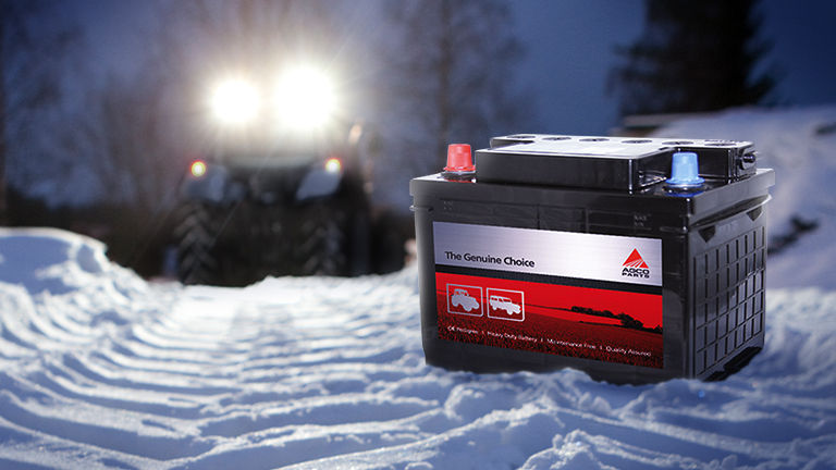 A tractor battery sitting on some snow with some headlights shining in the distance