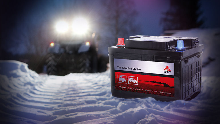 A batteries in the snow with tractor headlights behind it